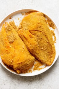 Two pieces of chicken with spices on a plate.