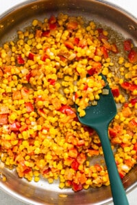 Corn in a pan with a green spatula.