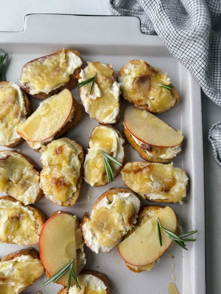 Cheesy roasted apple and goat cheese potato wedges with rosemary sprigs on a baking sheet, perfectly complemented by the aroma of roasted garlic.