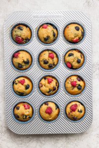 Muffins in a muffin tin with raspberries and blueberries.