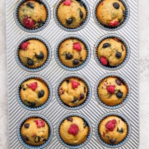 Muffins in a muffin tin with raspberries and blueberries.