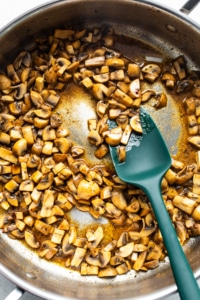 Mushrooms in a pan with a green spatula.