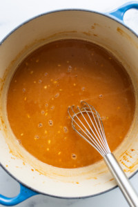 A pot of sauce with a whisk in it.