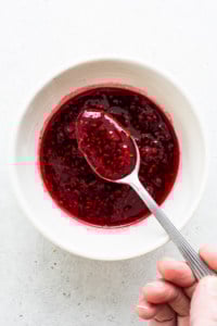 Raspberry jam in a white bowl with a spoon.