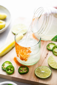 A person pouring a drink into a glass with limes and jalapenos.