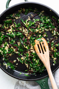 A skillet filled with greens and a wooden spoon.