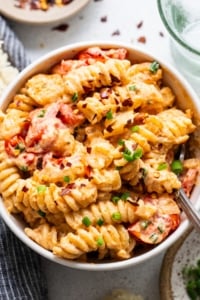 A bowl of creamy baked macaroni and cheese with sliced tomatoes and chopped green onions on top.