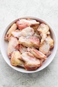 A bowl of raw chicken wings seasoned with spices.