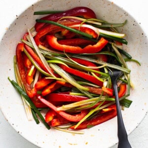 A bowl of sliced red bell peppers and green beans ready for cooking with Korean ground beef, accompanied by a spoon.