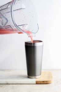Pouring a red smoothie into a metal tumbler.