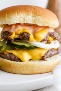 Close-up of a double cheeseburger with melted cheese, pickles, and onions.