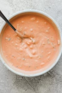 A bowl of creamy tomato soup with herbs, served with a spoon.