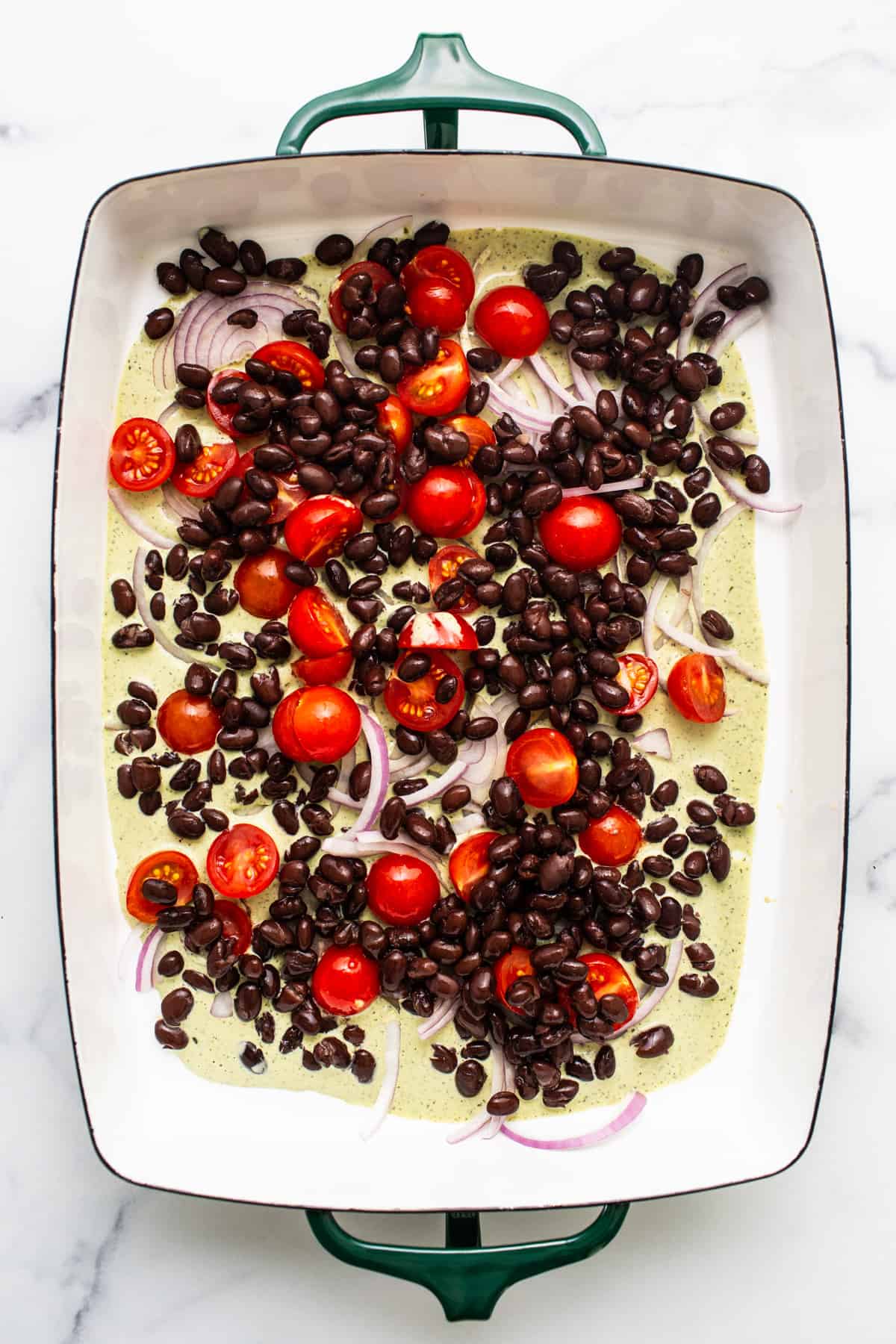 A baking dish with black beans, cherry tomatoes, and sliced onions, ready for cooking.