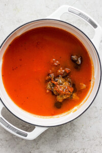 A pot containing tomato soup with herbs and vegetables visible on the surface.