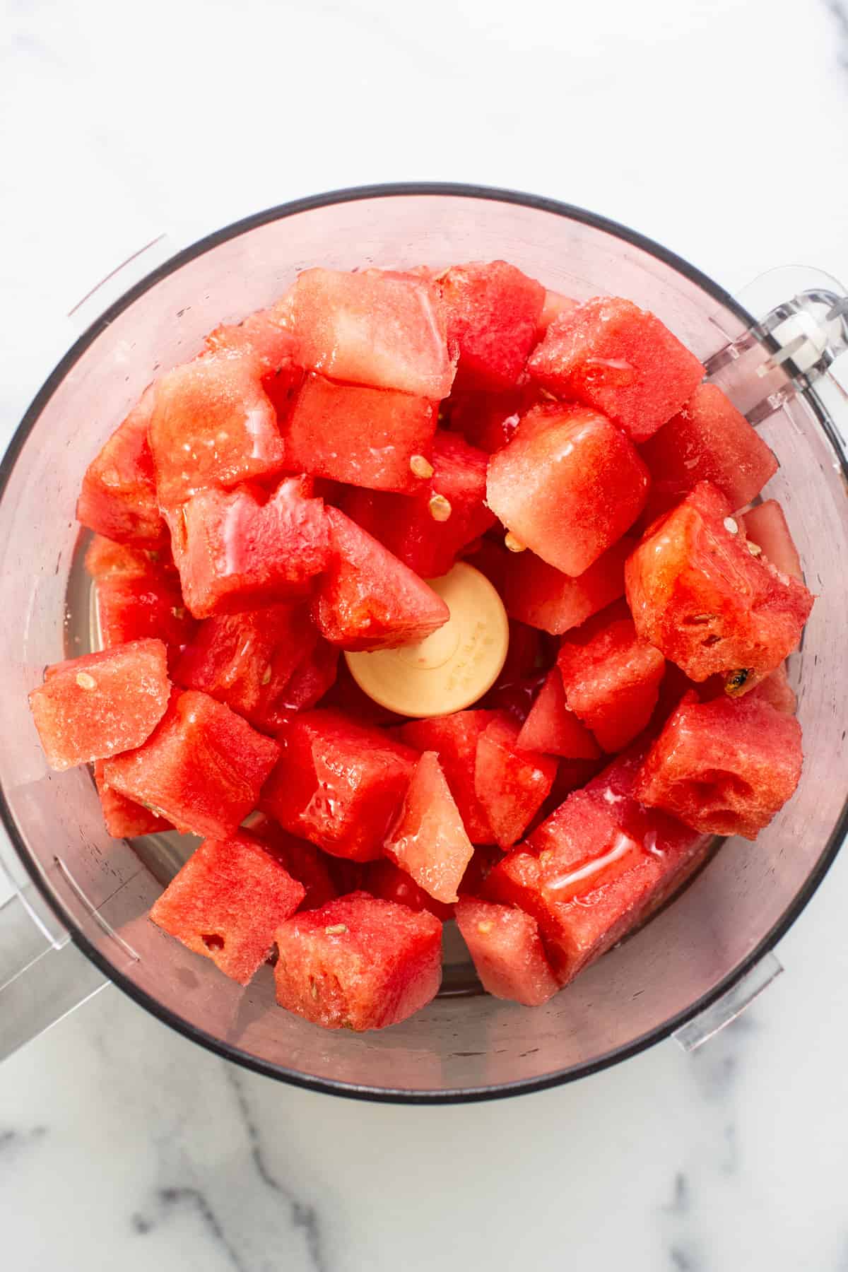 Chunks of fresh red watermelon in a food processor, ready for blending.