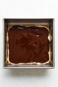 A square baking dish containing a layer of brownie topped with a glossy layer of chocolate ganache.