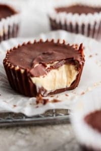 A close-up image of a chocolate peanut butter cup with a bite taken out, revealing creamy peanut butter filling. other cups in the background.
