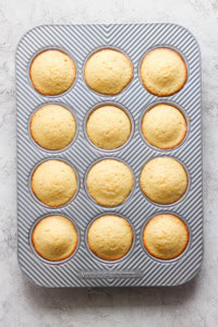 Freshly baked muffins in a 12-cup muffin tray with a striped pattern, viewed from above on a light surface.