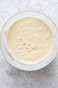 Top view of a glass bowl containing freshly prepared, smooth bread dough on a white surface.