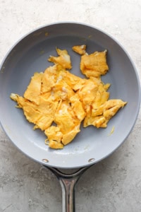 A non-stick frying pan containing scrambled eggs on a light-colored surface.