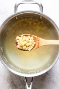 A wooden spoon holding macaroni noodles over a pot of boiling water.
