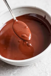 A spoon is held above a bowl of melted chocolate.