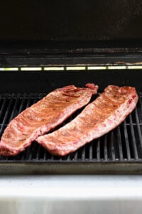 Two racks of seasoned ribs cooking on an open grill.