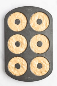 A six-cavity donut baking pan filled with unbaked donut batter, ready to be placed in the oven.