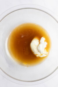 A glass bowl containing a mixture of liquid honey and a dollop of yogurt.