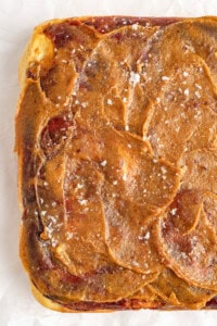 A close-up of a square piece of caramel-colored food that appears to be swirled with light and dark streaks and sprinkled with coarse salt on top.