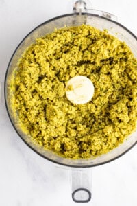 A food processor filled with blended green pesto.