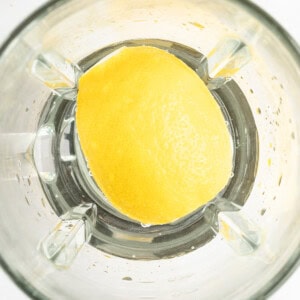 A halved lemon sits in a blender jar, viewed from above.