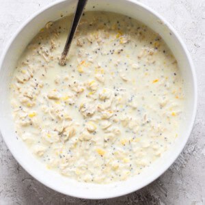 A bowl of oat mixture with chia seeds and grated lemon zest, reminiscent of creamsicle overnight oats, stirred with a spoon.