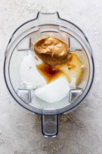 A blender containing yogurt, peanut butter, vanilla extract, and honey viewed from above evokes the creamy richness of a peanut butter banana ice box cake.