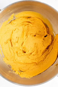 A stainless steel mixing bowl containing smooth, thick orange batter.