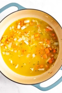 A pot of vegetable soup with chopped onions, carrots, and broth, simmering on the stovetop.