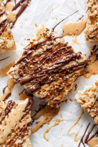 Close-up of toasted rice Krispie treats dessert bars topped with caramel and chocolate drizzle on a parchment paper background.