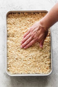 A hand pressing down on a tray filled with warm, toasted Rice Krispie treats mixture.