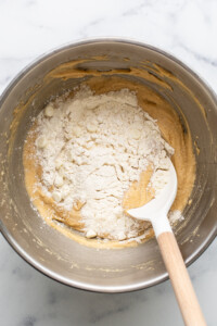 A mixing bowl containing partially mixed cookie dough with flour and white chocolate chips, resembling the beginnings of delectable strawberry blondies, and a white spatula resting inside.