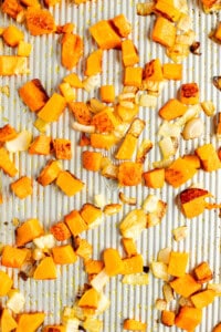 Diced butternut squash and chopped onions spread out and roasted on a baking sheet.