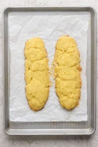 Two homemade almond biscotti cookie logs on a parchment-lined baking sheet.