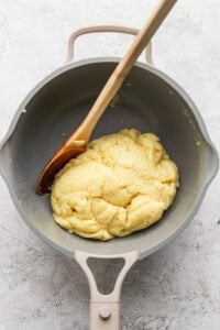 A wooden spoon rests in a pot containing a cooked dough mixture.
