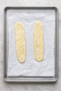 Two unbaked dough logs placed on a parchment-lined baking sheet, ready to be baked.