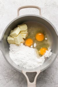 A mixing bowl containing flour, three eggs, and chunks of butter.