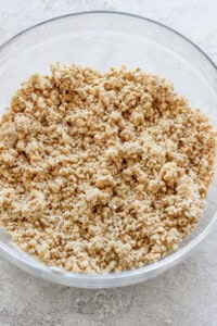 A clear glass bowl filled with a crumbly mixture, likely a streusel or crumble topping, on a light-colored countertop.