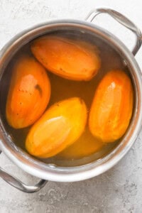 Four peeled sweet potatoes boiling in a stainless steel pot filled with water.
