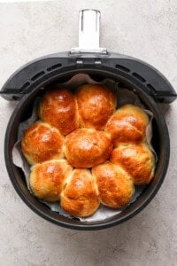 Golden brown homemade rolls arranged in a circular pattern inside an air fryer basket on a gray surface.