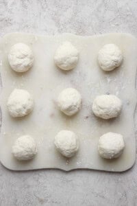 Nine dough balls on a floured surface, arranged in a 3x3 grid.