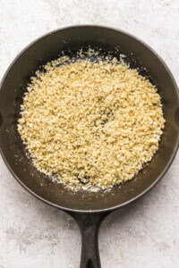 Crumbled cauliflower in a dark skillet on a light surface.
