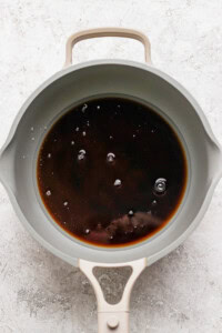 A gray pan containing dark liquid with a few bubbles on the surface, placed on a light gray textured background.